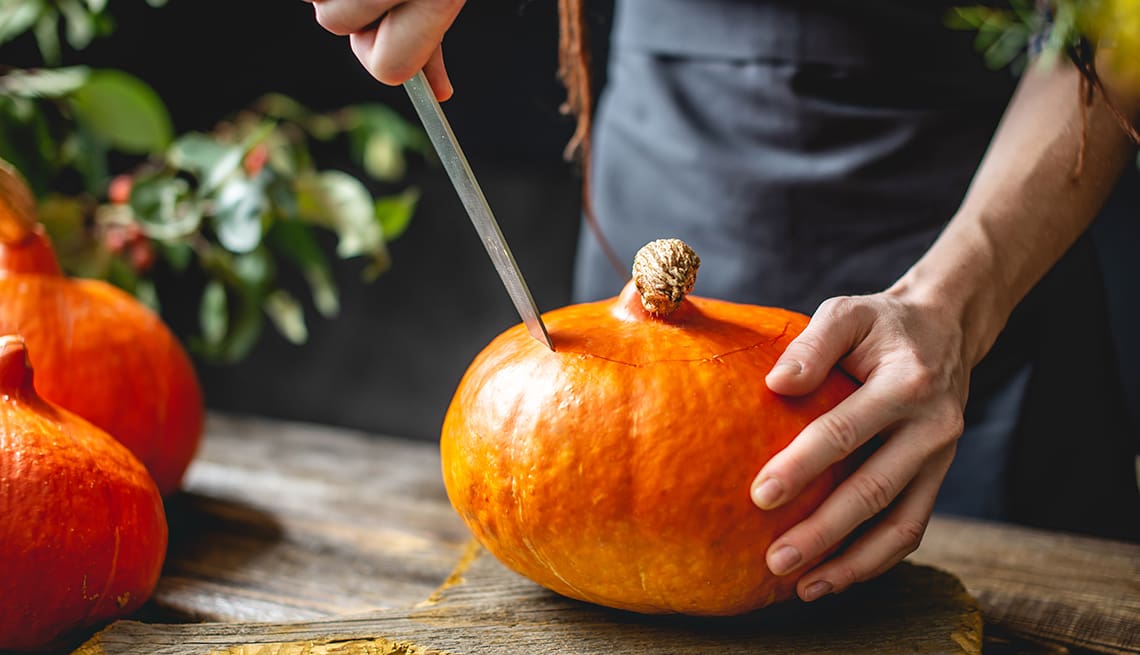 Woman chef cleans an orange pumpkin to prepare for baking. Autumn food in a cozy dark wooden kitchen with yellow flowers